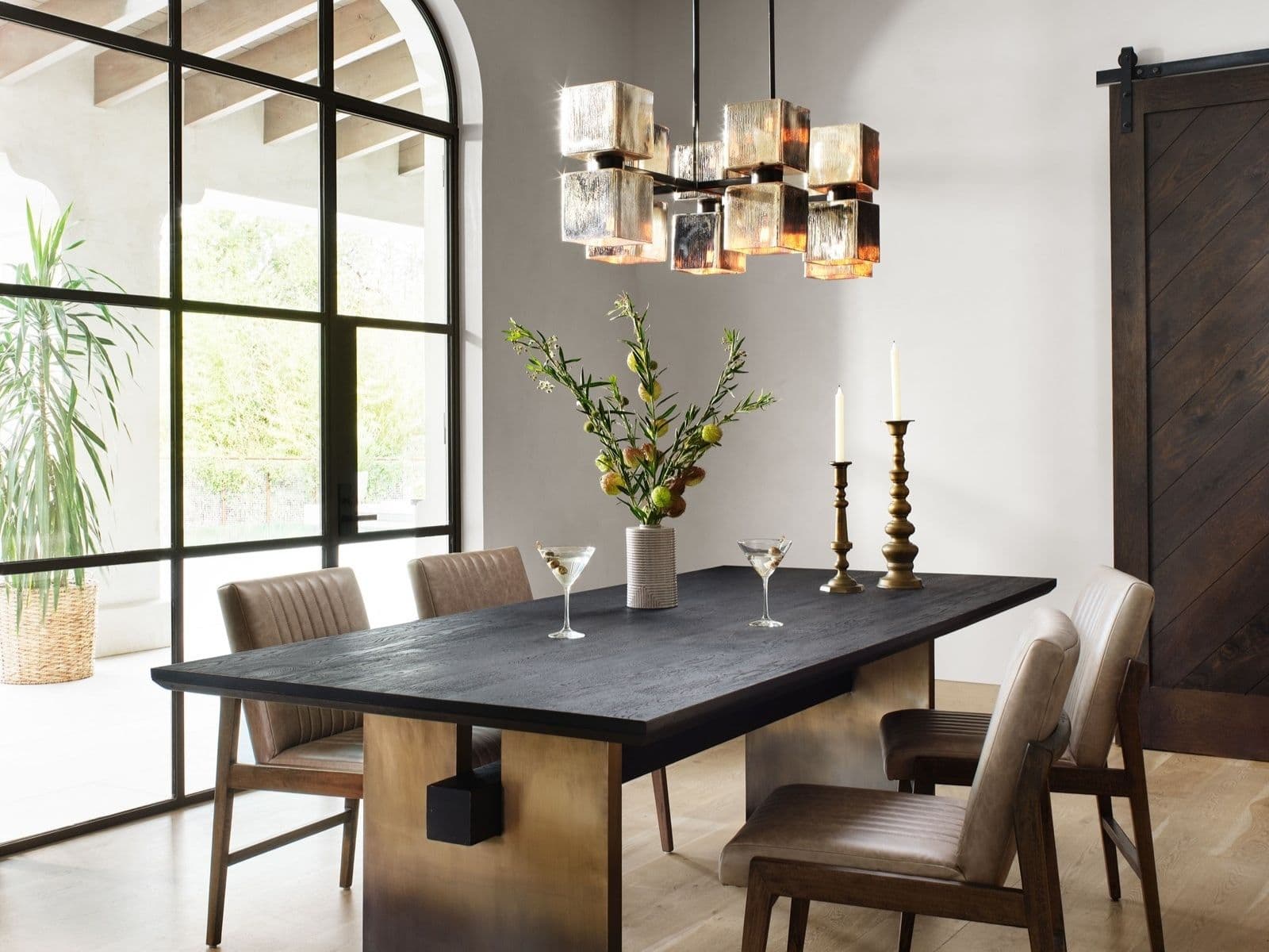Blackened oak dining table on brass plinths under a cubed glass chandelier